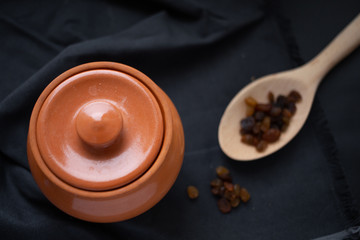 Brown pot with sour cream and a wooden spoon with raisins on a dark background.