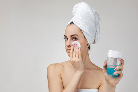Young woman in towel removing makeup from her face with cotton pad. girl using sponge and lotion for cleaning skin