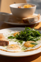 Tasty healthy breakfast: fried eggs, salmon, arugula and croutons on a white plate and  a mug of cappuccino on a wooden table.