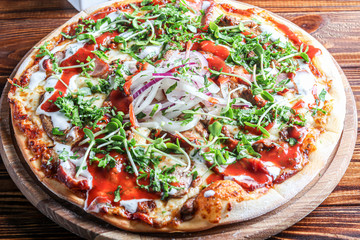 Pizza with bacon and herbs on a wooden plate with cheese and tomato sauce. On a dark background.