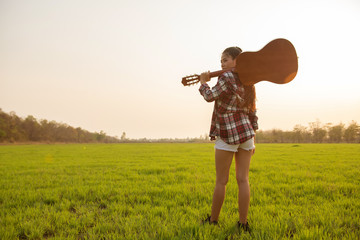 A beautiful woman with a guitar in the green meadow At sunset