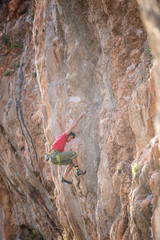 A strong man climbs a beautiful orange rock.