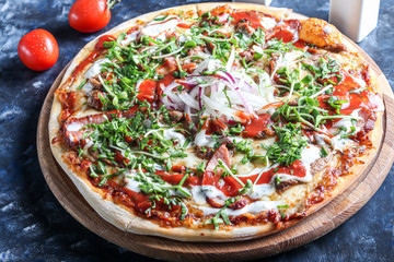 Pizza with bacon and herbs on a wooden plate with cheese and tomato sauce. On a dark background.