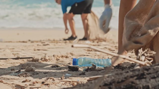 Closeup of two volunteers collects garbage at the white ocean beach intro garbage eco-bags, being socially active. Volunteering, charity and clean beach environment and tidying up rubbish concept