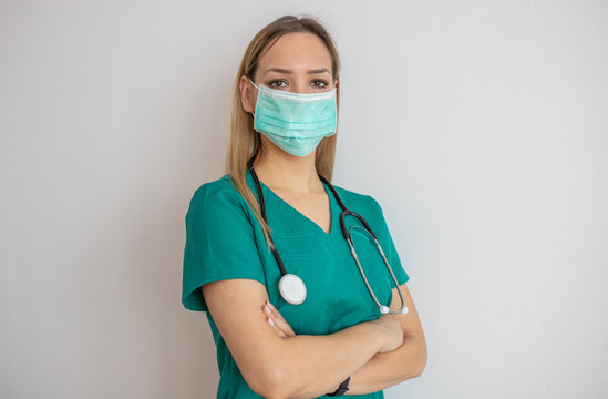 Female nurse standing arms crossed. Confident young woman doctor. Female nurse young pretty woman in green clothes with medical mask posing.