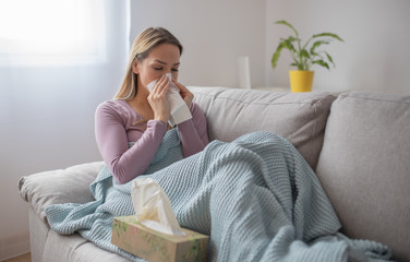 Sick woman blowing nose, sitting under the blanket. Sick woman with seasonal infections, flu,...