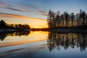 Sunset at lake with tree and cloud reflections, Sweden.