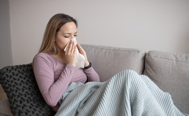 Sick woman blowing nose, sitting under the blanket. Sick woman with seasonal infections, flu, allergy lying in bed. Sick woman covered with a blanket lying in bed with high fever and a flu, resting.