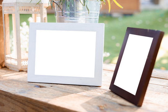 White and dark brown decorated photo frame with white background on outdoor wooden table.