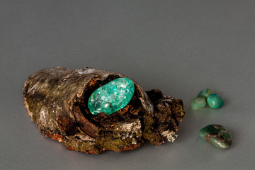 One shiny celadon color stone inside birch tree hollow and some gemstones outside. Gray background nad copy space for text.