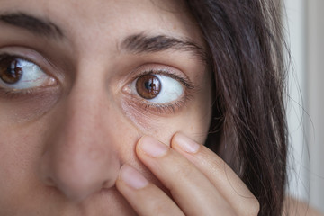 Close up of brown eye and dark circle of a young brunette caucasian girl touching her face, concept of dark circles and wrinkles, natural beauty
