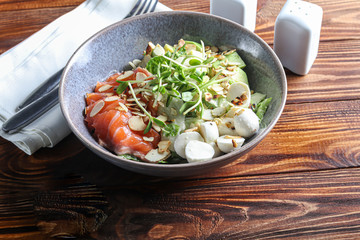 Salad of slightly salted salmon, avocado, mozzarella, microgreen and peanut slices. On a dark background.