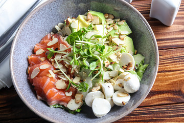 Salad of slightly salted salmon, avocado, mozzarella, microgreen and peanut slices. On a dark background.