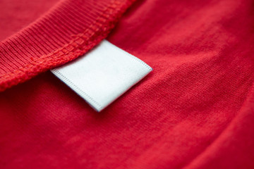 White blank clothing tag label on new red cotton shirt fabric texture background