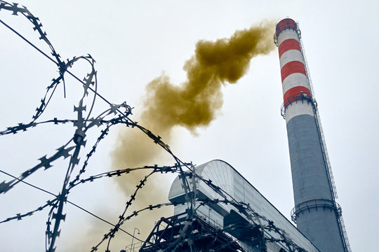 High hazardous factory chimney emits dense puffs of toxic green smoke into the environment. Territory of the factory is fenced with barbed wire.