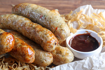 Chicken sausages with herbs and pita bread. On a wooden board. Mustard and ketchup sauces. On a dark background.