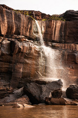 Large Sand stone canyon cliff shoreline and waterfall pouring onto Mekong river