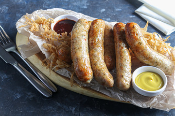 Chicken sausages with herbs and pita bread. On a wooden board. Mustard and ketchup sauces. On a dark background.