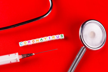 Pandemic and virus concept - Coronavirus text with syringe and phonendoscope on red background. Novel coronavirus Covid-19.