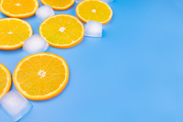 Orange slices and ice cubes on a blue background. Copy space.