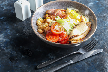 Caesar salad of grilled chicken tomatoes, lettuce, crackers and eggs. Healthy diet. On a dark background.