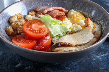 Caesar salad of grilled chicken tomatoes, lettuce, crackers and eggs. Healthy diet. On a dark background.