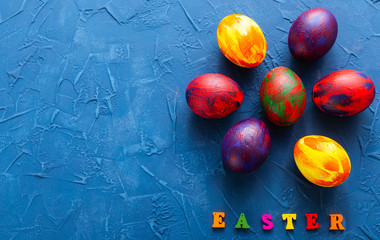 Fototapeta na wymiar Multi-colored wooden letters making up the words happy easter and decorative colourful eggs on a blue background with copy space.