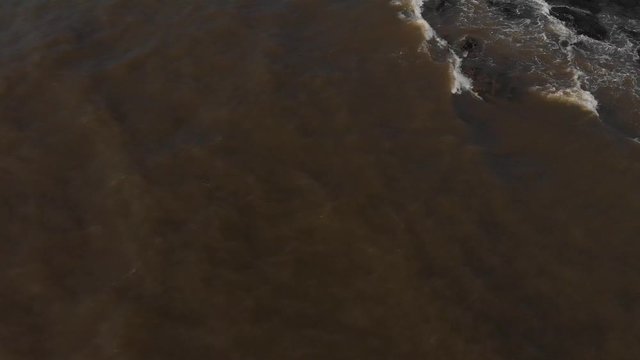 Drone shot panning up from a brown, dirty ocean to a flock of seagulls and then to the Large imposing Mumbai Skyline