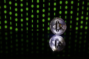 Bitcoin coin with reflection on black background with green binary code 