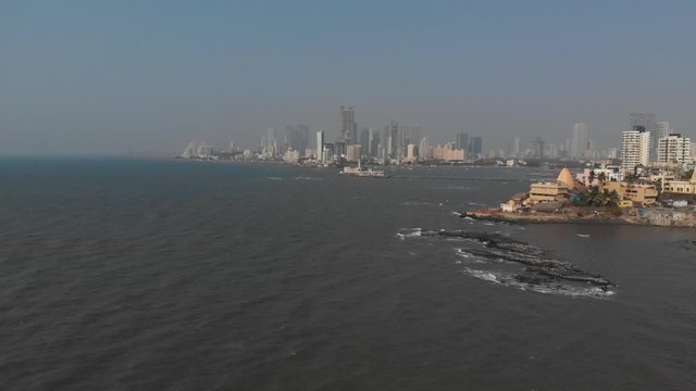 Falling drone shot of large buildings behind a hindu temple on the coast of Mumbai India
