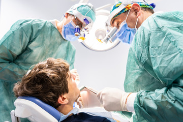 Professional dentist surgeon and assistant performing dental operation in a clinic with modern...