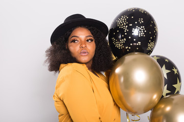 Naklejka premium Holidays, party and fun concept - Portrait of smiling young African-American young woman looking stylish on white background holding balloons.