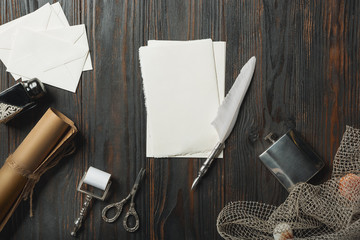 Old fashioned flat lay with letters writing accessories on dark wooden background. White sheets, pen, signet, package, ink. Vintage style, steampunk, gaslight concept. Magnifying glass and compass.