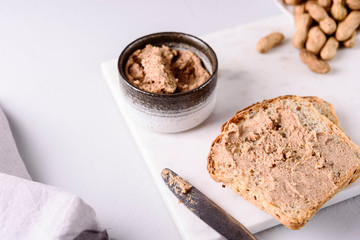 Homemade peanut paste or butter in a bowl and bread and peanuts on white marble tray. Healthy nutrition. Selective focus