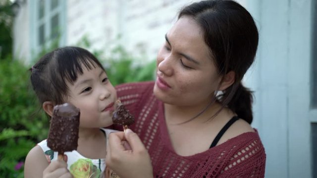 Little Asian Girl And Mother Eating Ice Cream Together Happily. Mother And Daughter's Happy Moments, Happy Family Concept. Handheld Shot And Real Life.	