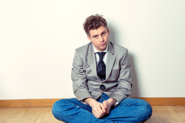 Portrait of a sad man sitting in a suit on the floor in his house