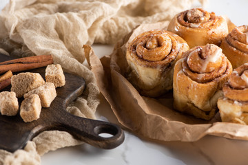 selective focus of fresh homemade cinnamon rolls near cutting board with brown sugar and cinnamon sticks