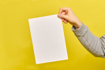 Copy space. Man hands holds a white paper sheet on a yellow background.