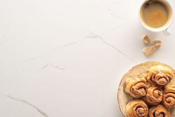 top view of fresh homemade cinnamon rolls on marble surface with cup of coffee, brown sugar