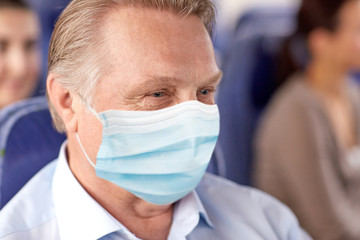 transport, tourism and pandemic concept - close up of senior male passenger wearing protective medical mask for protection from virus sitting in travel bus or airplane