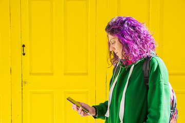 Young woman with purple hair listening to music leaning against a yellow door