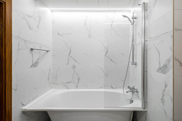 Modern contemporary bathroom in apartment. White bath and shower. Marble tile.