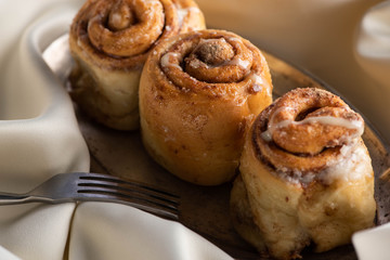close up view of fresh homemade cinnamon rolls on board on satin cloth with fork