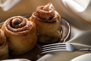 close up view of fresh homemade cinnamon rolls on board on satin cloth with fork