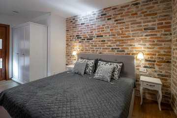 Modern contemporary loft interior of bedroom. Brick walls. Cozy bed with pillows. Wardrobe.