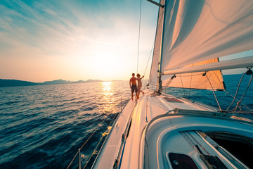 Young couple enjoys sailing in the tropical sea at sunset on their yacht. - 330948241