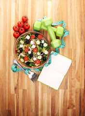 Authentic fresh salad in a stone cup with dumbbells excercise equipment, measuring tape on table. healthy lifestyles, good health Concept with fresh ingredients