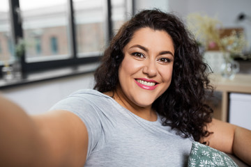 people, technology and leisure concept - happy smiling young woman taking selfie at home