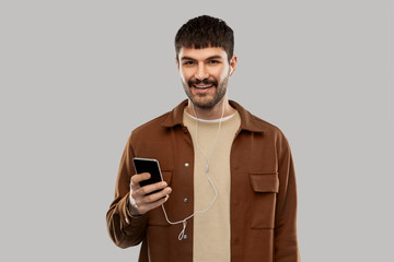 music, technology and people concept - smiling young man with earphones and smartphone over grey...
