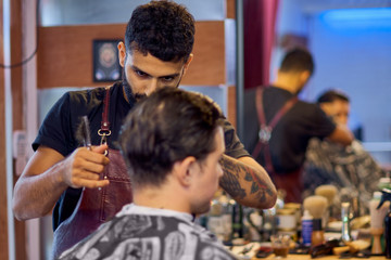 Master cuts hair and beard of men in the barbershop, hairdresser makes hairstyle for a young man